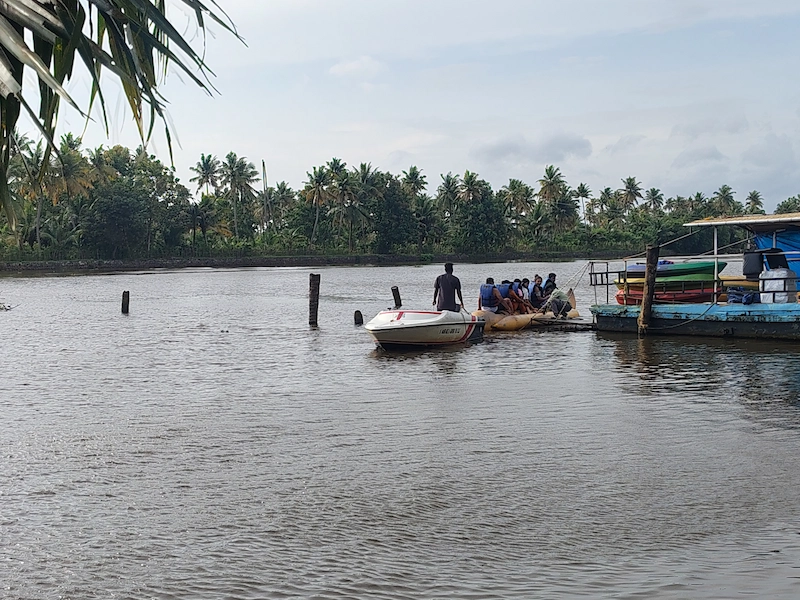 Houseboat cruising along water edge with palm trees in Kumarakom backwaters Kerala