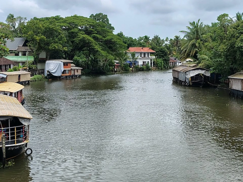 Traditional houseboat cruising along quiet backwater river lined with lush tropical greenery in Kerala